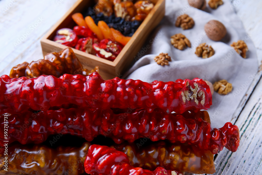 Board with delicious churchkhela and box of ingredients on white wooden background