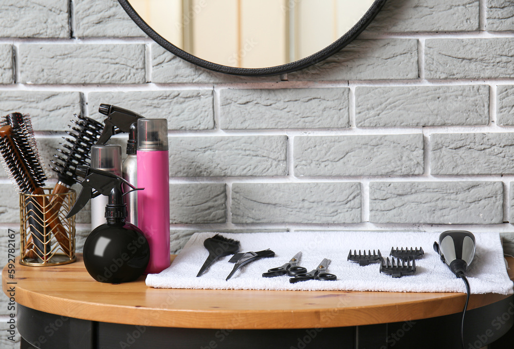 Different hair sprays and accessories on table near grey brick wall