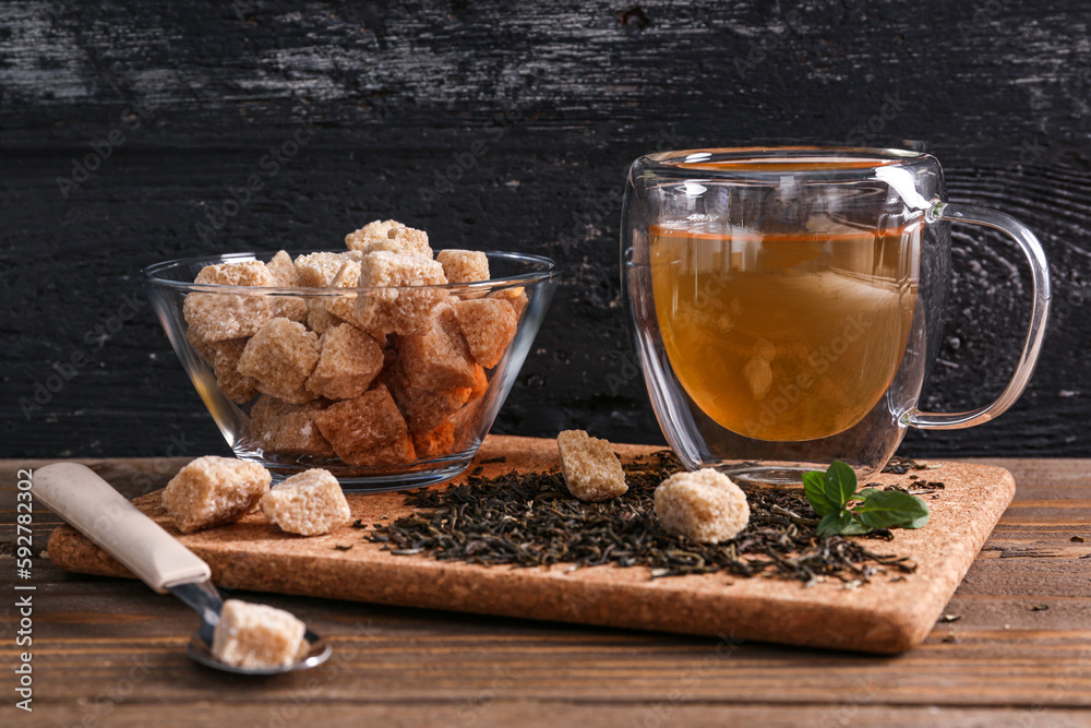 Cup of hot green tea with sugar and dry leaves on table