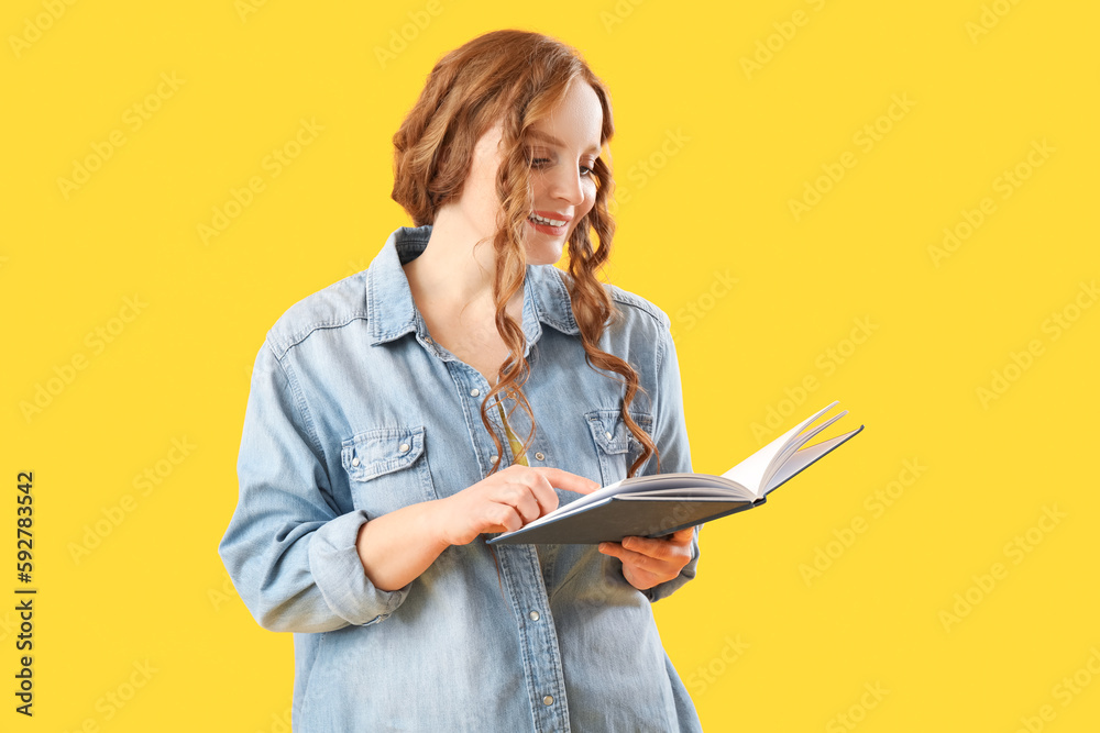 Beautiful redhead woman reading book on yellow background