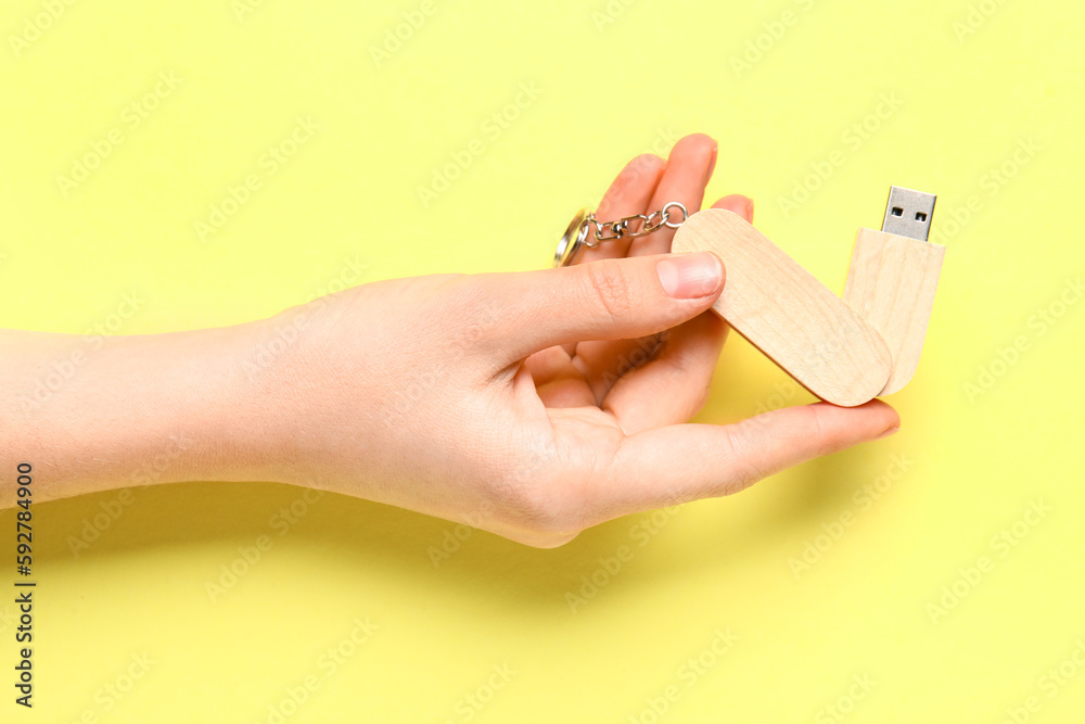 Woman holding wooden USB flash drive on yellow background