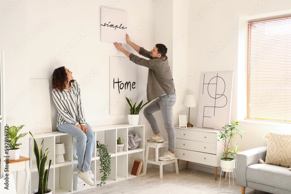 Young couple hanging poster on light wall at home