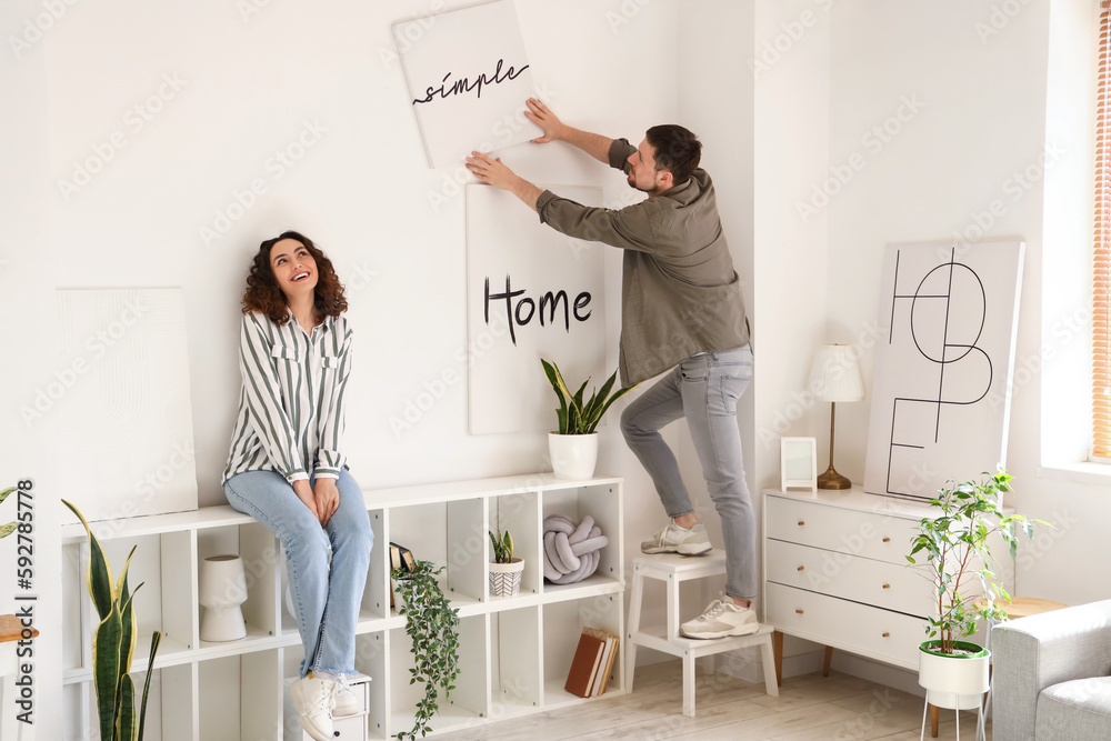 Young couple hanging poster on light wall at home