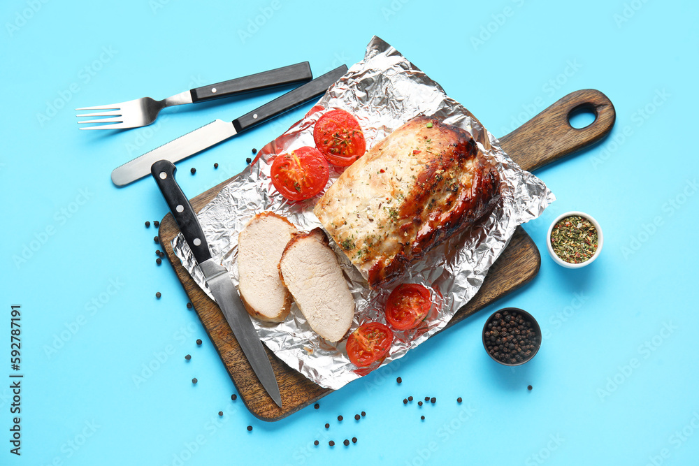 Wooden board with tasty baked meat, tomatoes, spices and cutlery on color background