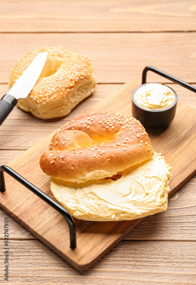 Board of tasty bagels with sesame and cream cheese on wooden background