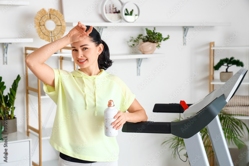 Beautiful woman with bottle of water after training on treadmill at home