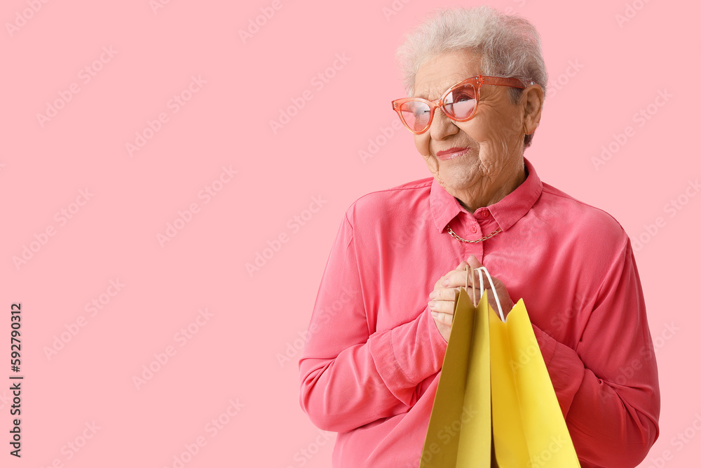 Senior woman with shopping bags on pink background