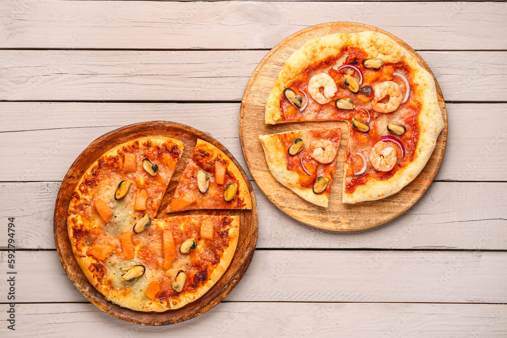 Plates of tasty seafood pizza on light wooden background