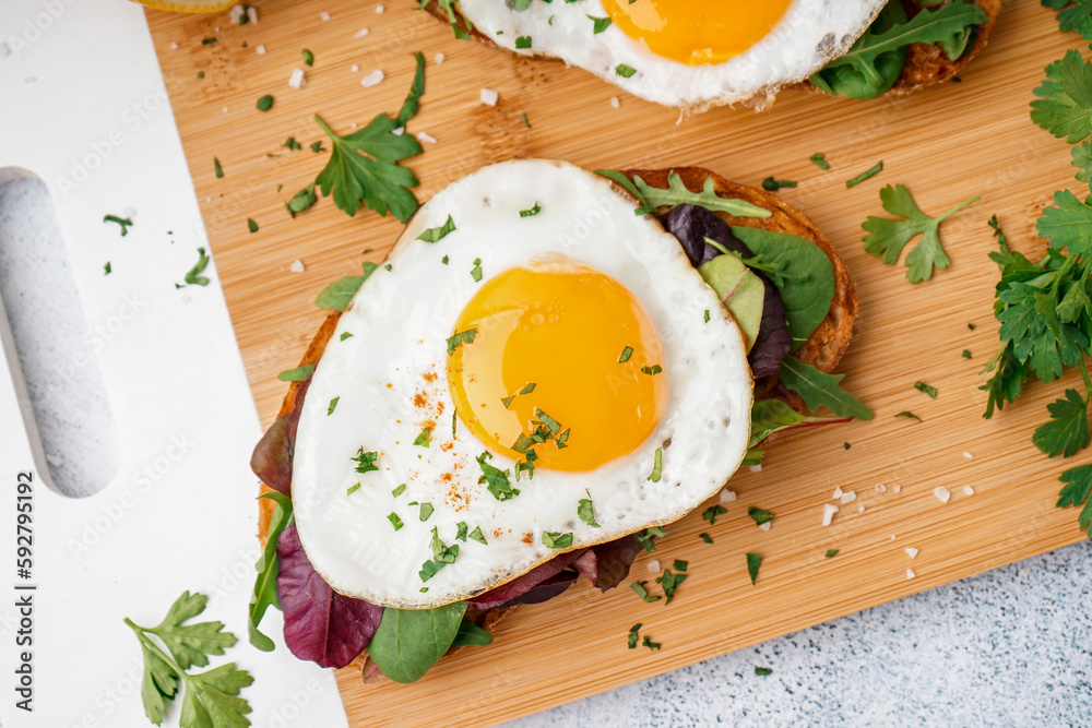 Delicious sandwiches with fried eggs on light background