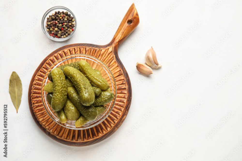 Bowl with tasty fermented cucumbers, wooden board and ingredients on white background