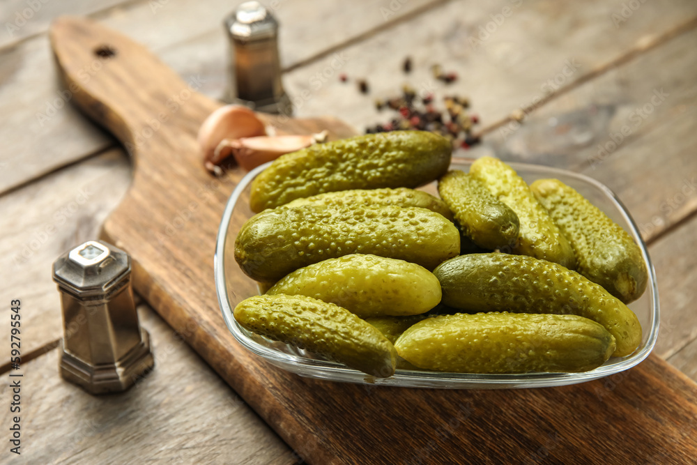 Bowl with tasty fermented cucumbers, ingredients and board on wooden background