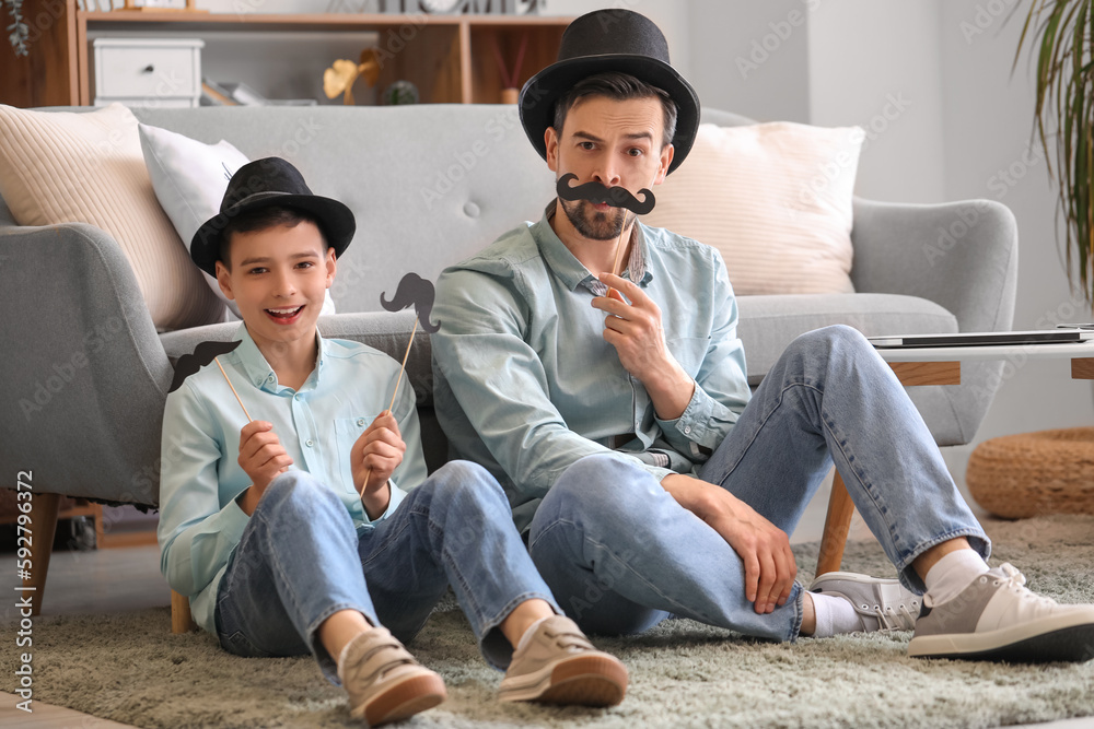 Portrait of father and his little son with paper mustache at home