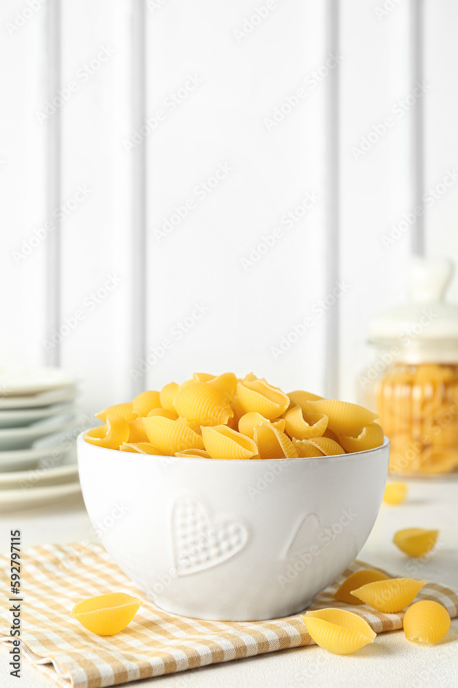 Bowl with raw conchiglie pasta on light background