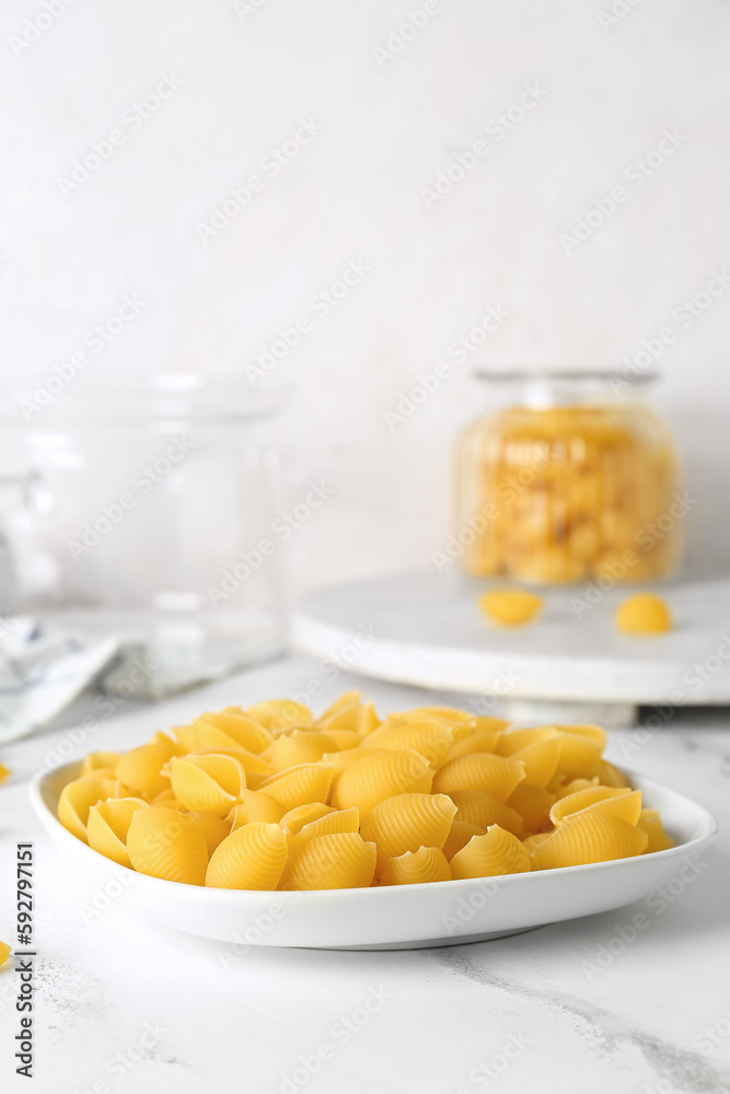 Plate with raw conchiglie pasta on light background