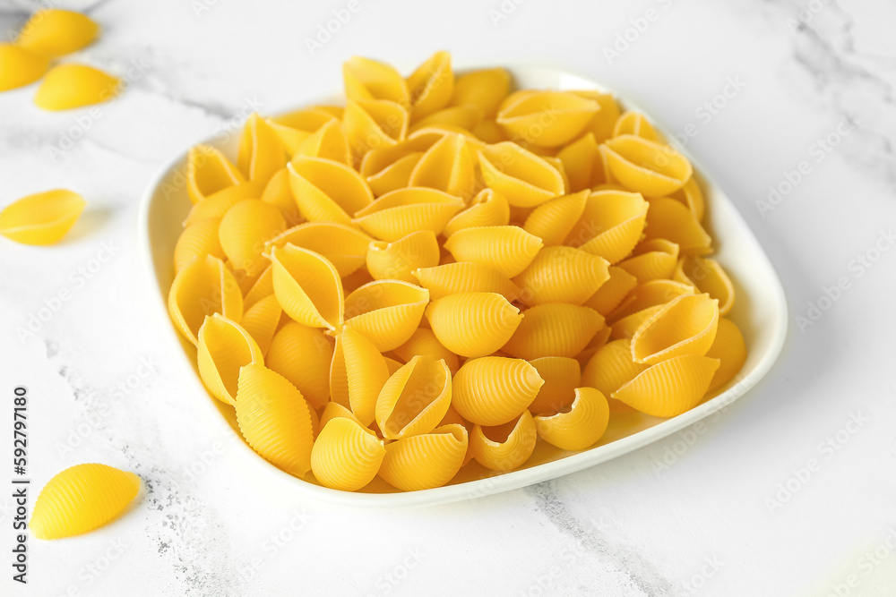 Plate with raw conchiglie pasta on white marble background