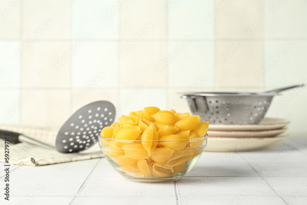 Bowl with raw conchiglie pasta on white tile background