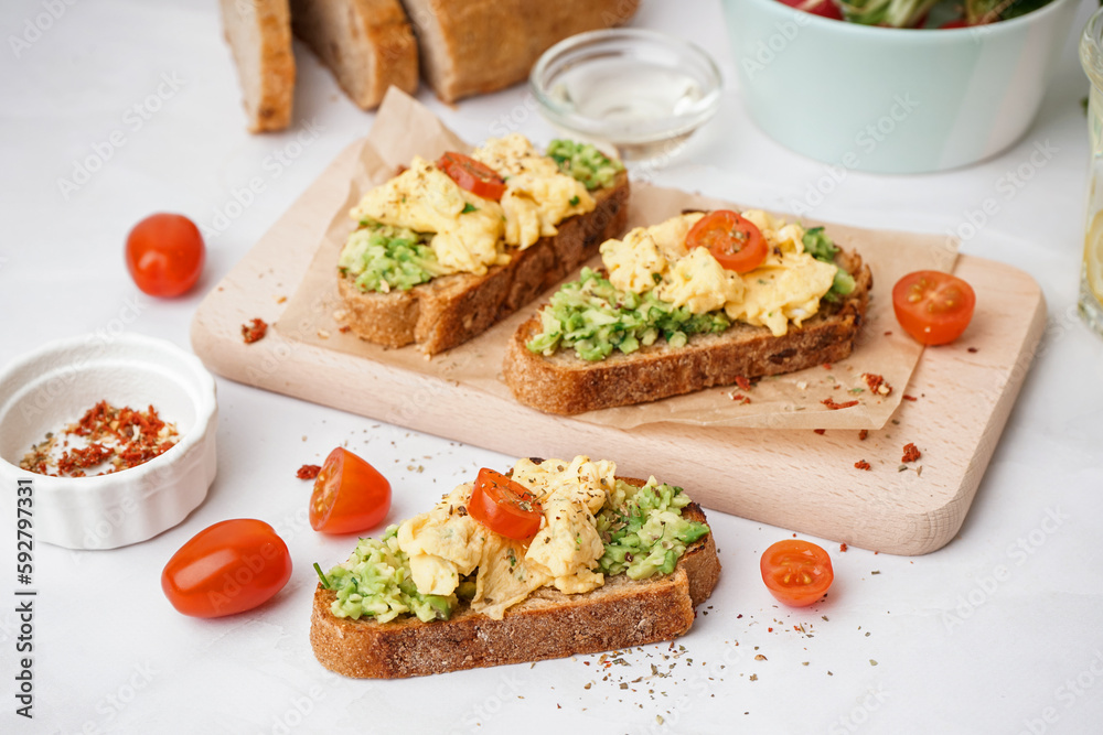 Wooden board with tasty scrambled eggs sandwich and vegetables on light background