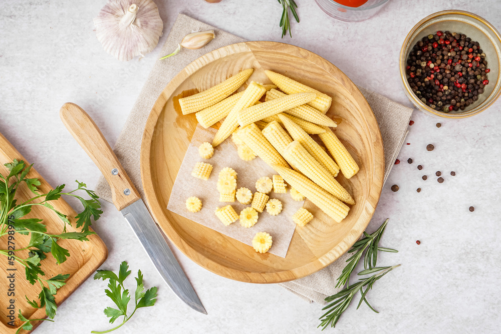 Plate with cut and whole canned baby corn cobs on light background