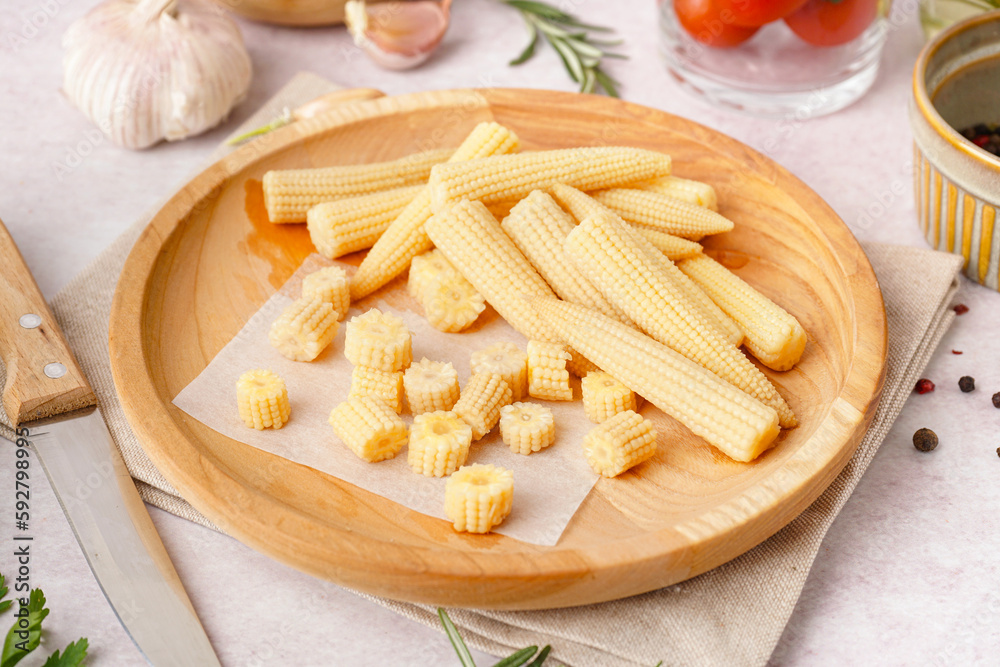 Plate with cut and whole canned baby corn cobs on light background