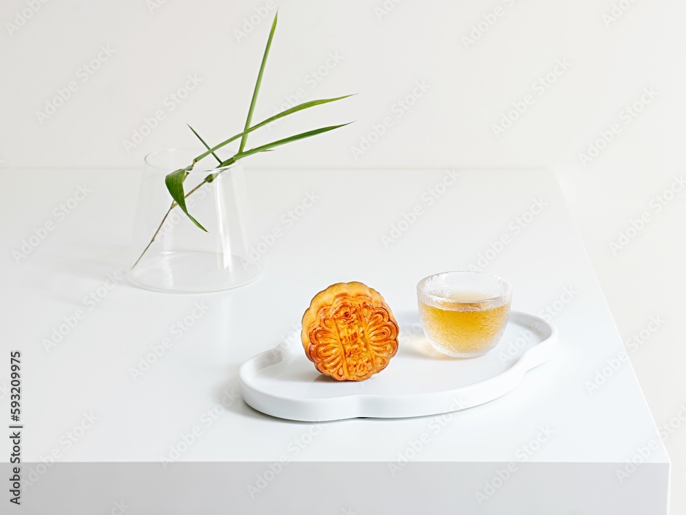 Close-up shot of a mooncake, a teacup in white plate and a decorative plant on a table