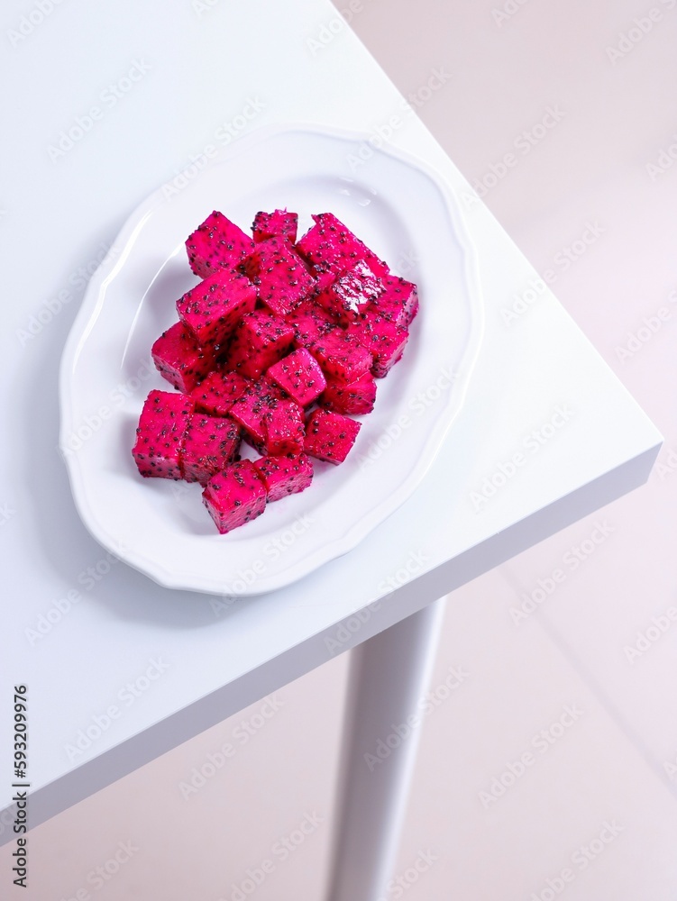 Vertical shot of pink dragon fruit cut in cubes in a white plate on a table