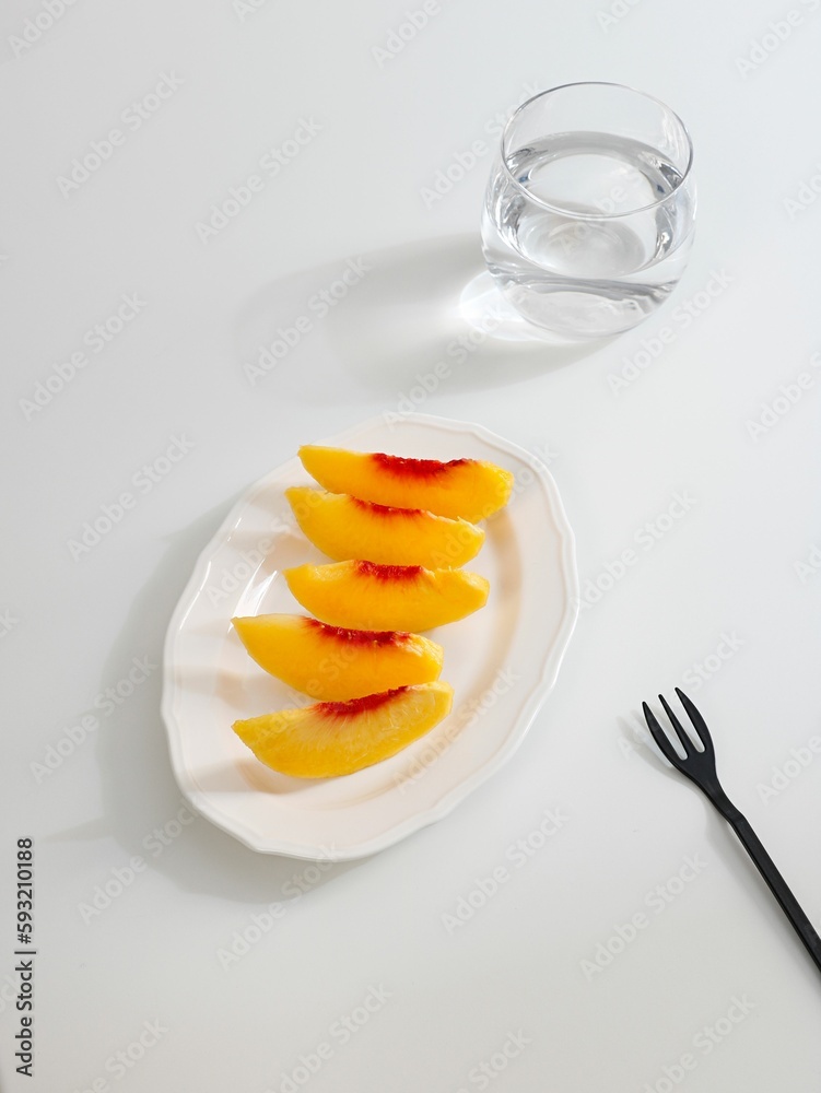 Flat lay of cut peach slices on a white plate with a minimalistic table set