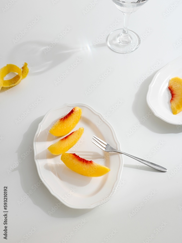 Flat lay of cut peach slices on a white plate with a minimalistic table set