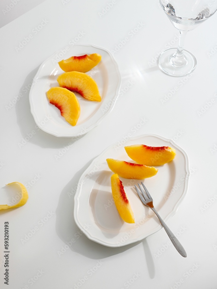 Flat lay of cut peach slices on white plates with a minimalistic table set