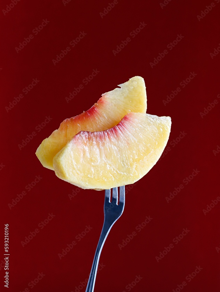 Closeup of peach slices on a fork in a maroon background