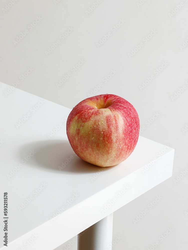 Close-up shot of a red apple on the corner of a white table