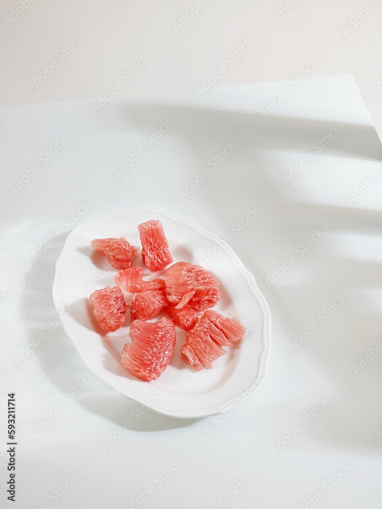 Vertical shot of a plate of red pomelo pieces on a white table