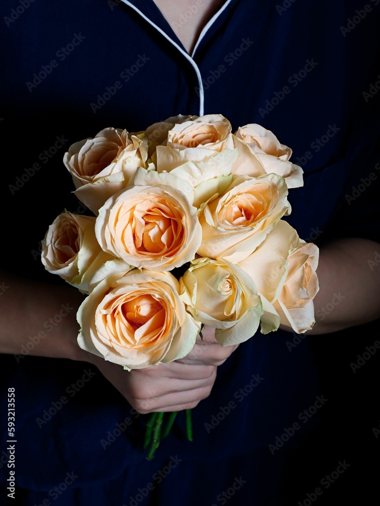 Vertical shot of a woman holding a bouquet of colorful roses in a studio in a dark background