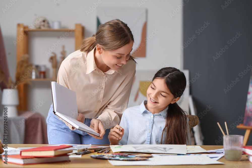 Drawing teacher with book giving private art lesson to little girl in workshop