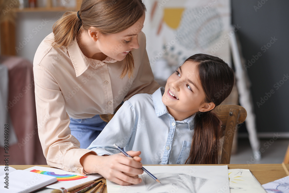 Drawing teacher with pencil giving private art lesson to little girl in workshop