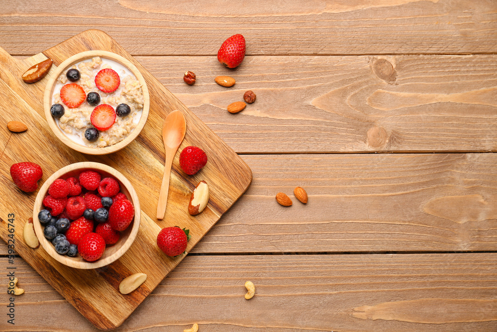 Bowls with tasty oatmeal, ripe berries and nuts on wooden background