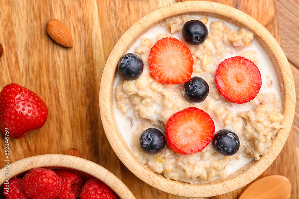 Bowl with tasty oatmeal, blueberries and strawberries on wooden background