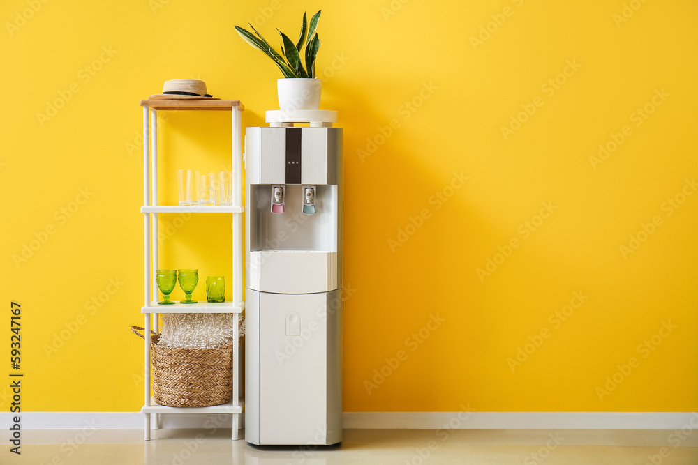 Modern water cooler and shelving units with glasses near yellow wall