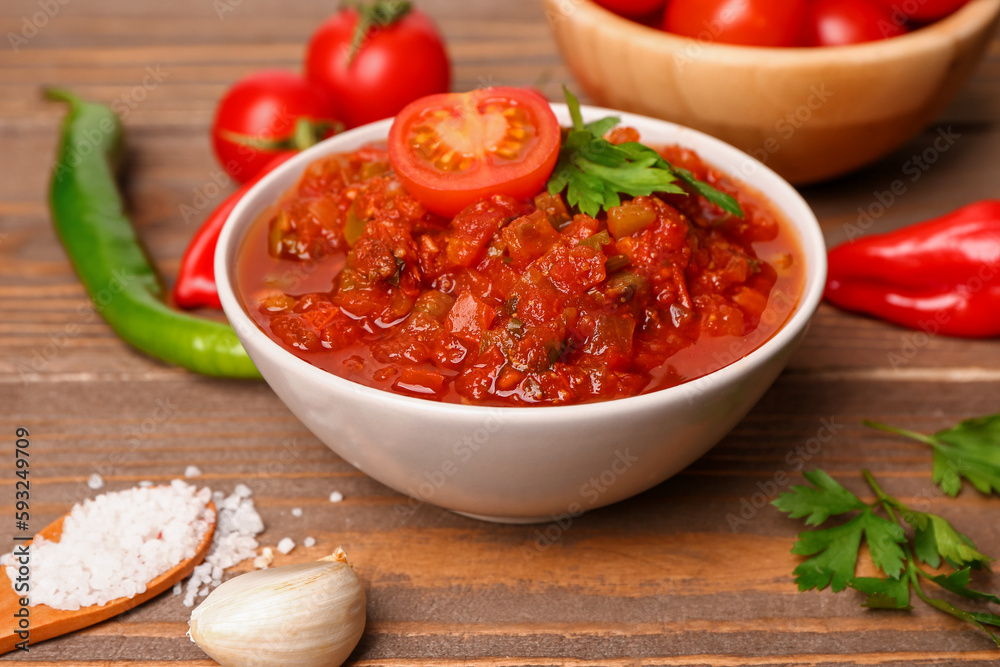 Bowl of delicious salsa sauce and ingredients on brown wooden table