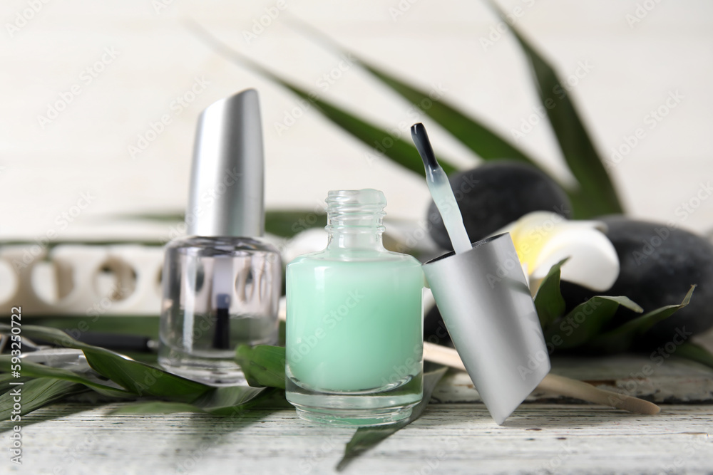 Bottles of cuticle oil and palm leaf on light wooden table, closeup