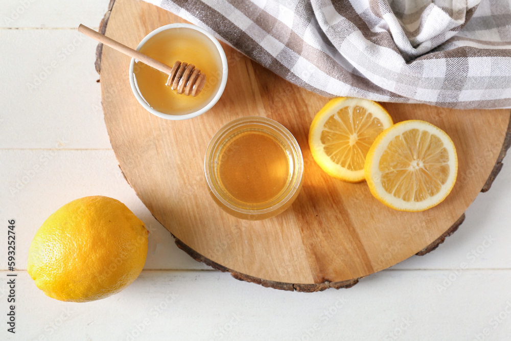 Jar and bowl of sweet honey with lemon on light wooden background