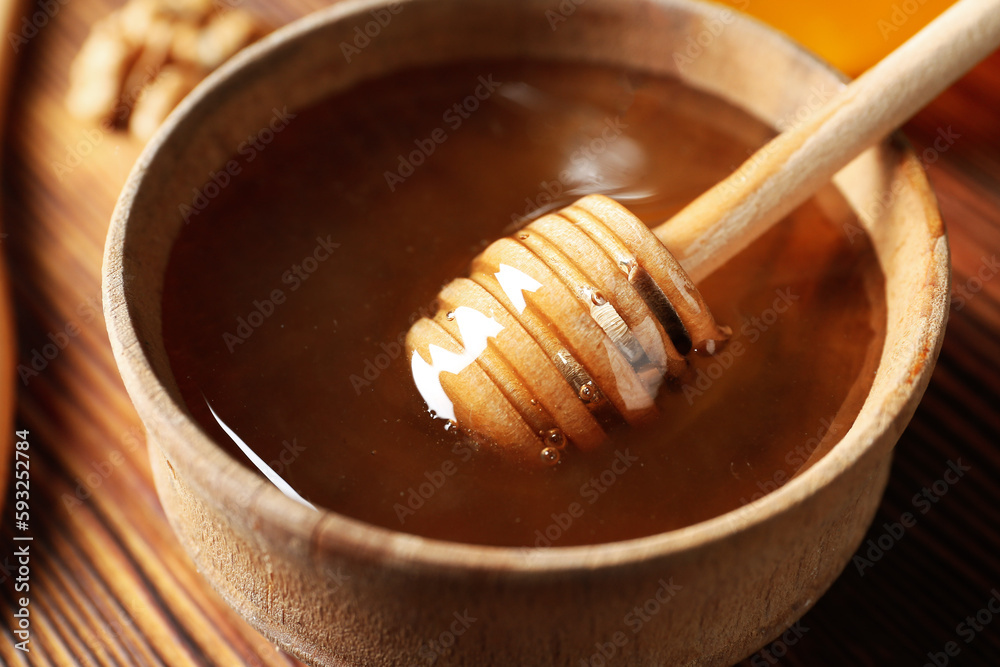 Bowl of sweet honey with dipper on wooden background, closeup