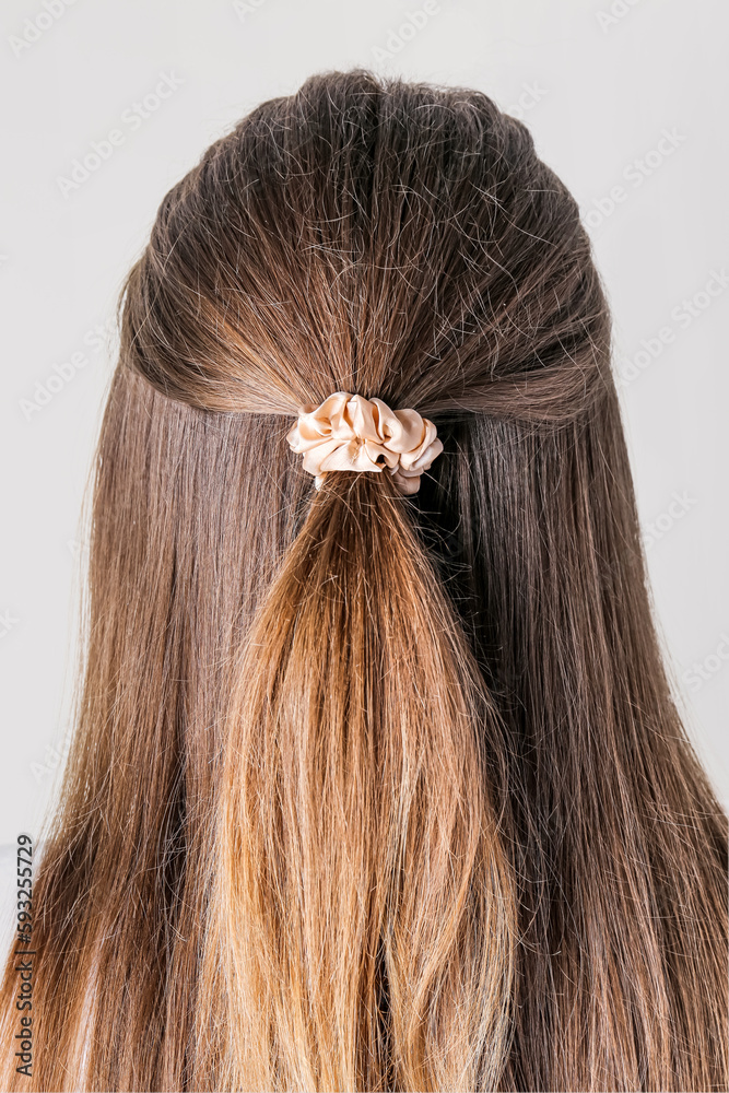 Woman with stylish hairdo and silk scrunchy on light background, back view