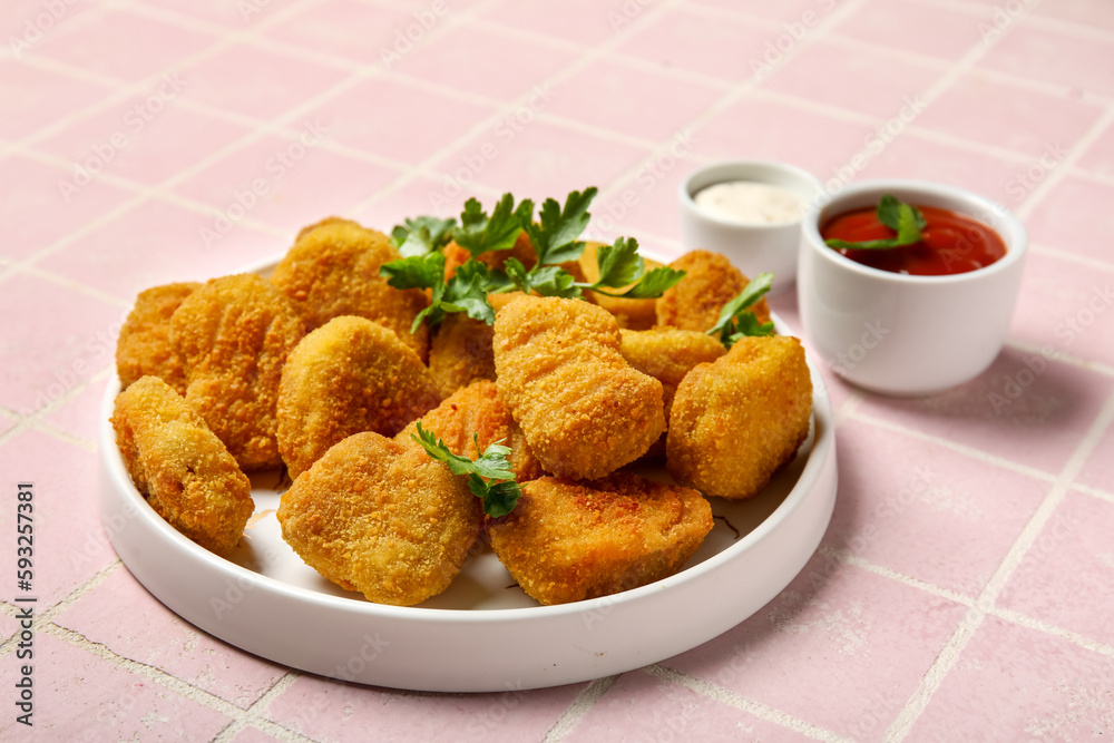 Plate of tasty nuggets on pink tile background