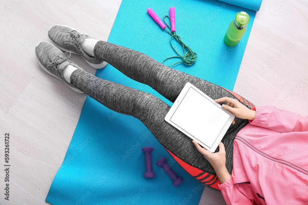 Sporty woman with tablet computer sitting on mat in gym