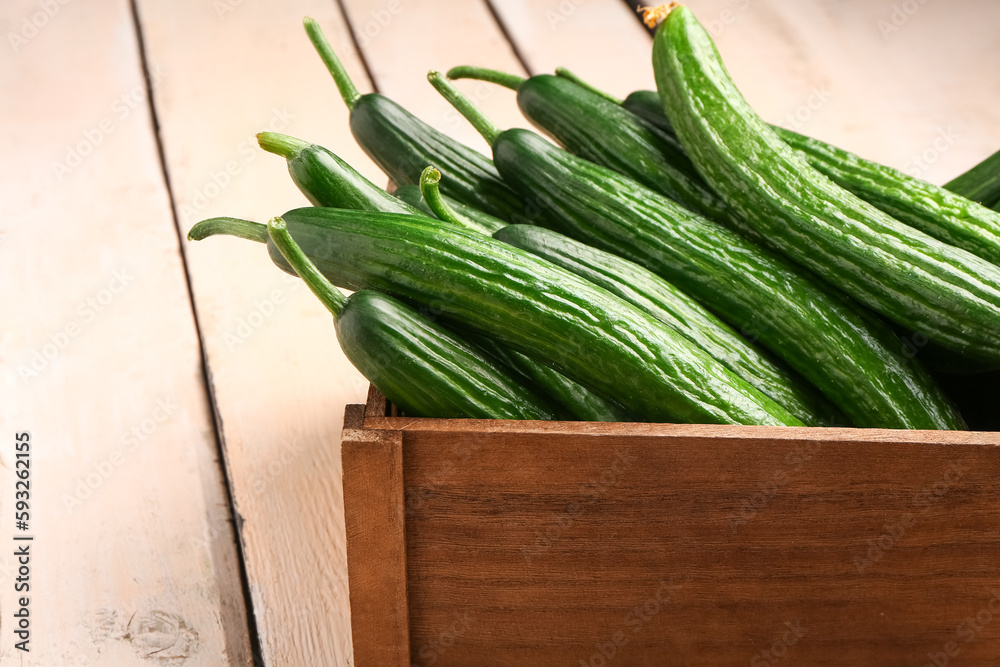 Box with fresh cucumbers on light wooden background, closeup