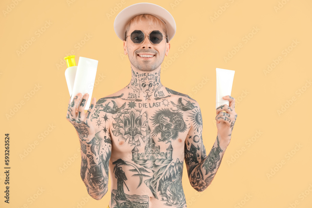 Tattooed man with sunscreen creams on beige background