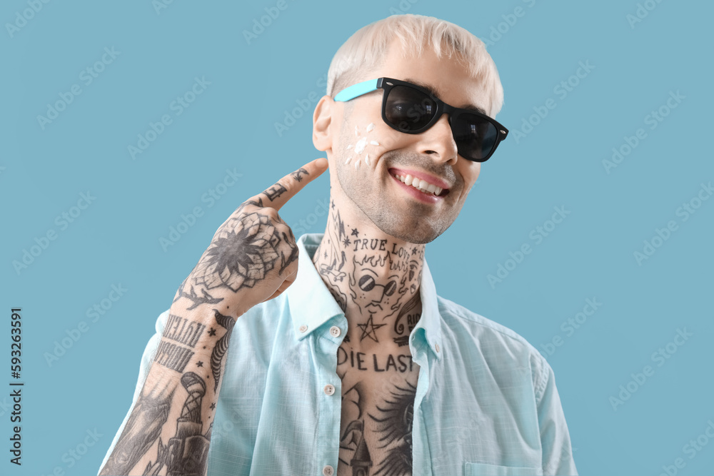 Tattooed man with sunscreen cream on his face against light blue background