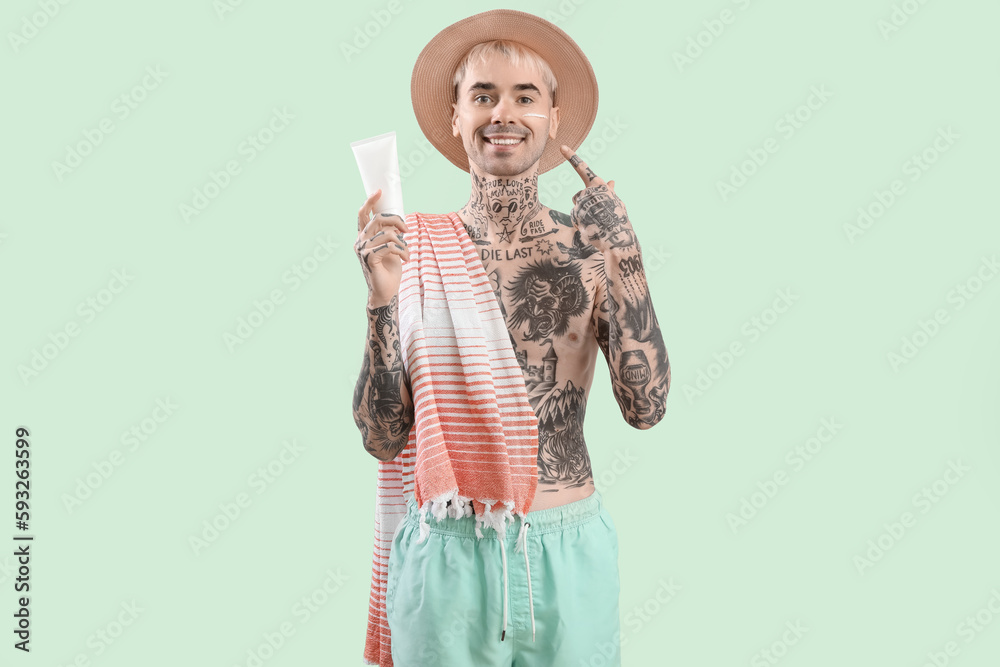 Tattooed man with sunscreen cream on light green background