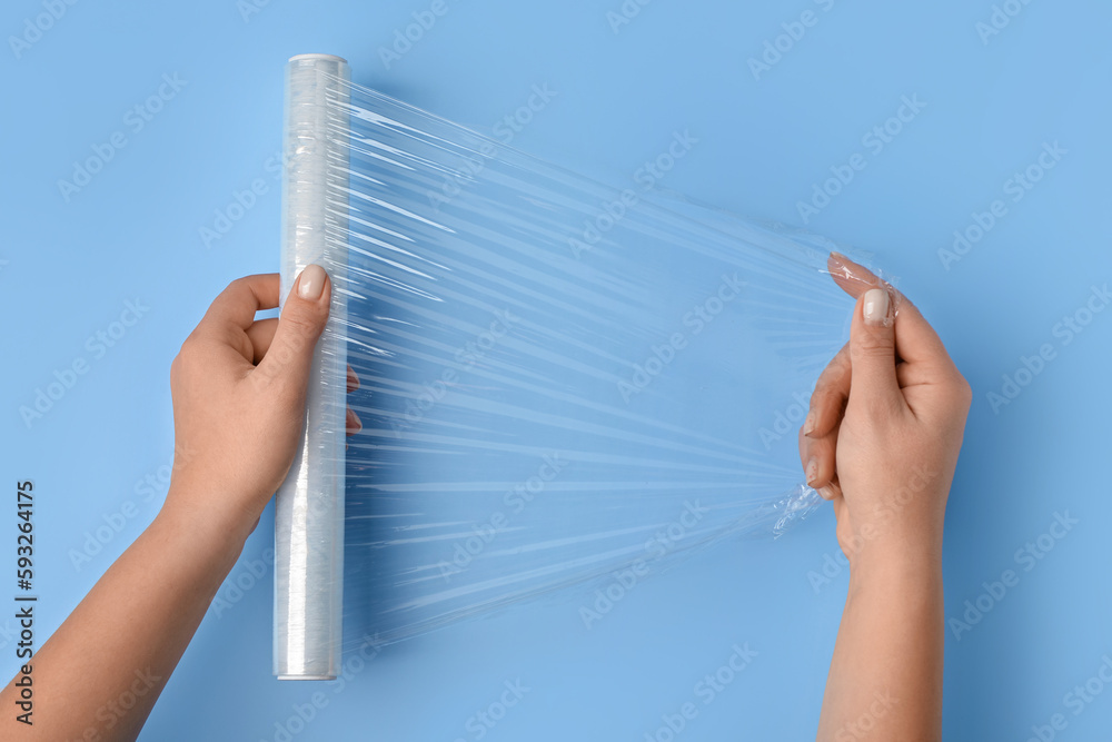 Female hands with roll of stretch wrap on blue background