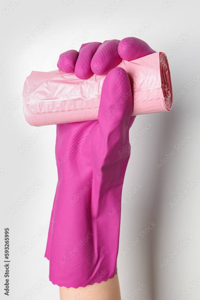 Hand in rubber glove with roll of garbage bags on white background